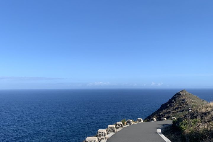 Paved path along a coastal cliff with ocean and clear blue sky in background.