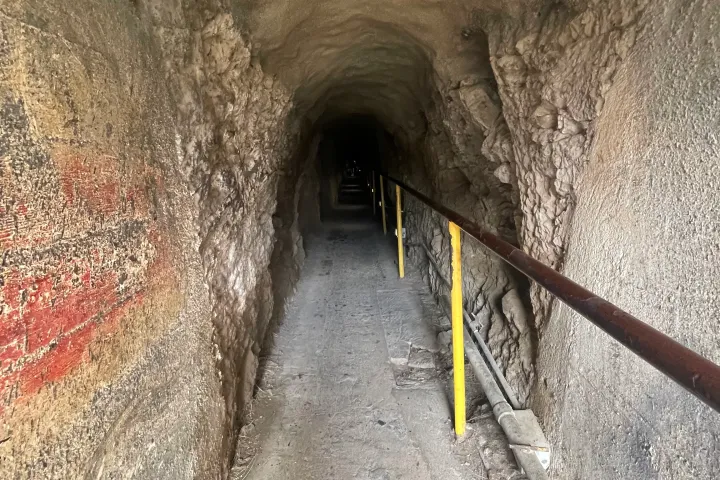 Narrow rock tunnel with handrails and a dimly lit path.