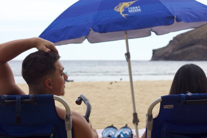 a group of people sitting at a beach umbrella in the sand